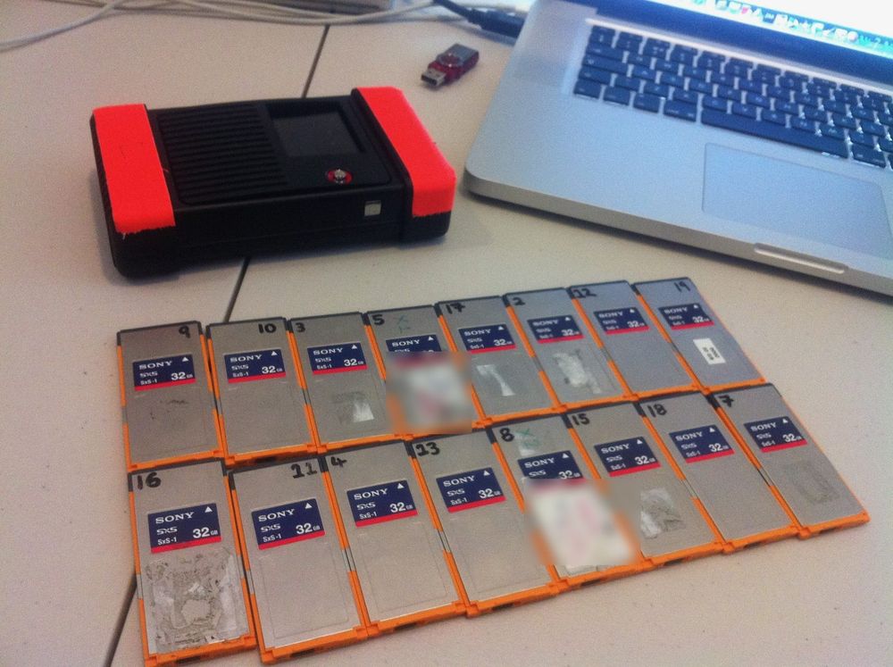 Two rows of numbered Sony SxS memory cards beside a card reader and a laptop.